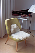 Abgenutzter grüner Vintage-Stuhl mit Schafsfellvorleger im Musikzimmer