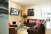 Braunes Ledersofa mit wandmontiertem Fernseher im Wohnzimmer eines flippigen Hauses in London, England, Vereinigtes Königreich