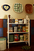 Detail von altem Küchengeschirr und Dosen auf offenen Regalen in der Küche mit an der Wand hängenden Tellern