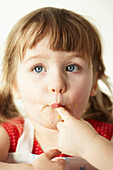 Drei Jahre altes Mädchen mit blauen Augen sitzt und lutscht an ihrem Finger