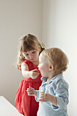 Young girl in red dress helping her brother to eat a biscuit