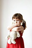 Junges Mädchen in rotem Kleid hält einen Teddybär