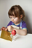 Kleines Mädchen klebt goldene Sterne auf ein gefärbtes Osterei