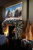 Open fire burning with large festive garland draped over the mantlepiece and candles burning on the hearth