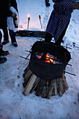People stand near barbecue grill with burning embers in snow, Zermatt, Valais, Switzerland