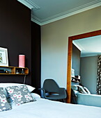 Schlafzimmer mit dunkler Wand und großem Wandspiegel und Sessel