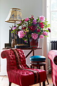 Red upholstered chair with cut flowers on side table in Cumbrian farmhouse, England, UK