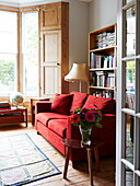 Rotes Sofa und Erkerfenster im Wohnzimmer eines farbenfrohen Hauses in London, England, Vereinigtes Königreich