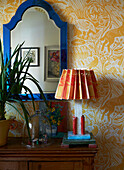 Handmade lamp with bright mirror frame and patterned wallpaper in London home, England, UK