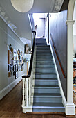 Painted staircase with wooden banister and framed artwork in hallway of Rye family home, East Sussex, England, UK