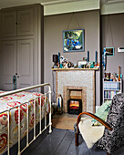 Tiled fireplace with armchair and footboard in bedroom of Rye family home, East Sussex, England, UK