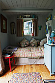 Floral cushions on single bed quilt below window of Rye summer house, East Sussex, England, UK