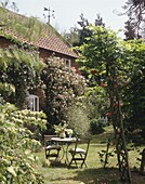 House exterior overgrown with flowers and plants with garden table and chairs