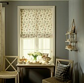 Fenster mit Fensterläden und geblümtem Raffrollo mit Konsolentisch mit weißen Blumen und Kleiderbürsten