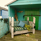 Wooden sofa with checked fabric cushions on decking of green painted beach house