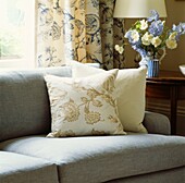 Cream cushions on light grey sofa with cut flowers and floral patterned curtains