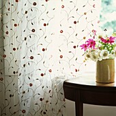 Vase of wildflowers on table at window with floral patterned curtains