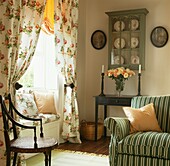 Floral patterned curtains at window seat in room with display cabinet and striped sofa