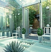Modern conservatory with glass flooring and double doors opening to walled courtyard exterior