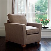 Light brown armchair at window with striped curtains and vase of roses on windowsill