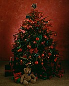 Teddy bear and gifts under Christmas tree decorated with green and red baubles