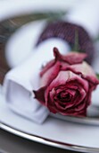 Gedeck mit einer dunkelrosa Rose neben einer weißen Serviette
