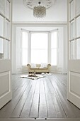 Minimalistisches weißes Zimmer mit cremefarbenem Ledersofa mit Knopfleiste in einem Erkerfenster mit cremefarbenem Whippet-Hund, der auf einem Ziegenfellteppich liegt und zur Tür schaut