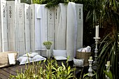 White folding screen in garden setting with bedlinen baskets and candlesticks