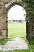 Blick durch einen gepflasterten steinernen Torbogen mit Tor zur Wiese