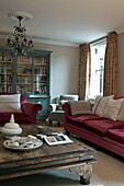 Niedriger Couchtisch aus Holz mit rotem Samtsofa und Sessel im Wohnzimmer eines modernen Hauses in Haywards Heath, West Sussex, England, UK