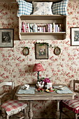 Floral wallpaper and wall mounted bookcase above table in tea salon,  Dordogne,  France