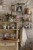 Wandmontiertes Metallregal und hölzerne Küchenkommode mit Tellern in einem Bauernhaus aus Stein, Dordogne, Frankreich