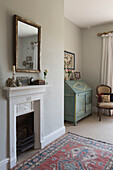 Gilt framed mirror above fireplace with writing desk and patterned rug in East Barsham cottage  Norfolk  England  UK