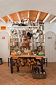Pfannenregal und Bücherregal mit Brennholz in einer terrakottagefliesten Küche, Castro Marim, Portugal