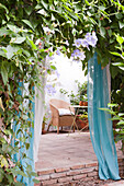 Wicker armchair on terrace with curtained entrance in Castro Marim courtyard, Portugal