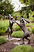 Statuen von zwei Hasen, die im Kräutergarten des Hauses in Amberley, West Sussex, England, UK, auf den Hinterbeinen miteinander kämpfen