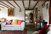 Vergoldetes gerahmtes Kunstwerk über einem weißen Sofa mit hellen Kissen in einem Cottage mit Balken in Devon, England, UK
