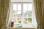 Gebundene Bücher auf der Fensterbank mit Blick auf den Garten in einem Bauernhaus in Petworth, West Sussex, Kent