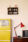 Red desk lamp with yellow cabinet and wall mounted shelf in Birmingham home  England  UK