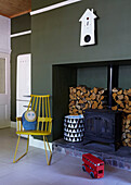 Wood burner recessed to green wall of London family home with yellow chair and toy bus,  England,  UK