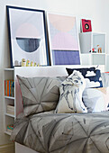 Kopfteilregal mit Kunstwerken und grauen Bettbezügen im Schlafzimmer einer Londoner Familie, England, UK