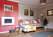 Red feature wall with print collection and colourful cushions in living room of Bolton home,  Greater Manchester,  England,  UK