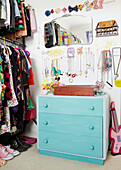 Colourful vintage clothes and necklaces hang with painted chest of drawers in dressing room of York home  England  UK