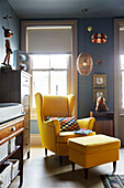 Yellow armchair and footstool with sash windows in East London townhouse  England  UK