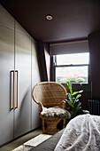 Wicker chair with built-in wardrobes in attic bedroom of East London townhouse  England  UK