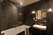 Mit dunklem Travertin gefliestes Badezimmer mit weißer Badewanne und Waschbecken
