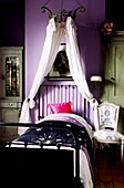 Girl's lilac bedroom with cast iron single bed and metal chandelier with muslin drapes