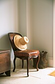 Still life of leather antique chair and straw hat in entrance hall