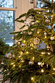 Christmas tree detail with glass and silver baubles and fairy lights against window