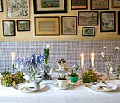 Hübsch gedeckter Tisch mit Kerzen, Hyazinthen- und Blumenzwiebel-Tischdekoration und alten Mustertüchern an der Wand